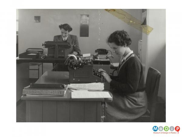 Scanned image showing two females sat at typewriters.