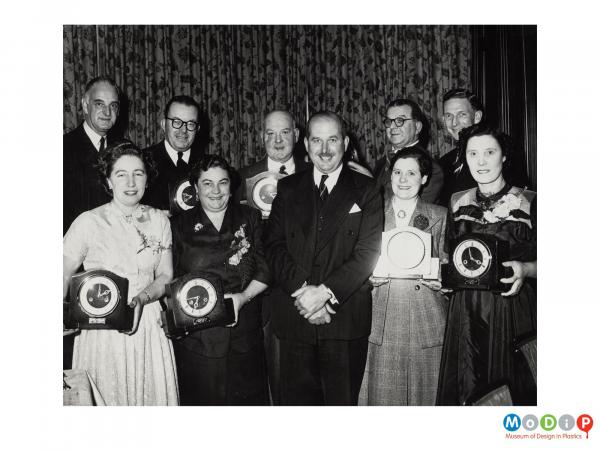 Scanned image showing a group of male and female workers holding mantle clocks.