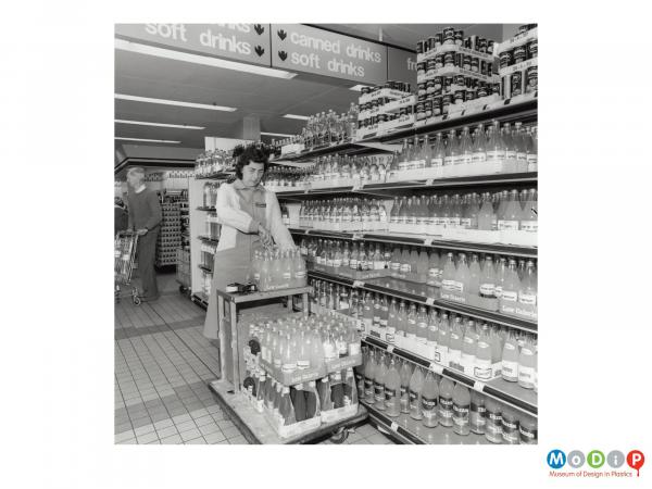 Scanned image showing a woman stacking shop shelves.