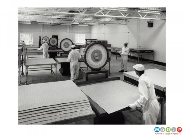 Scanned image showing several workers weighing sheets of material.