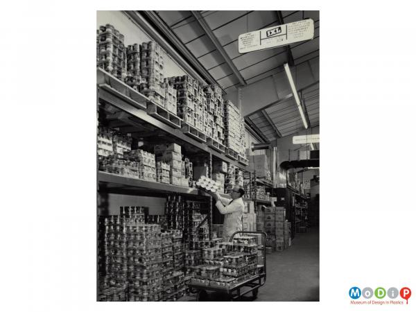 Scanned image showing shrink wrapped tins being stacked in a warehouse.