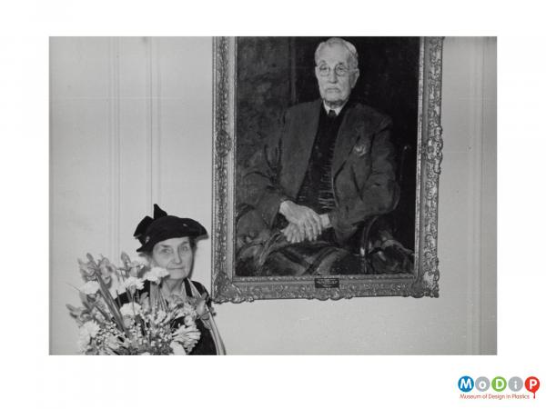 Scanned image showing a woman holding a bouquet flowers in front of a painting.