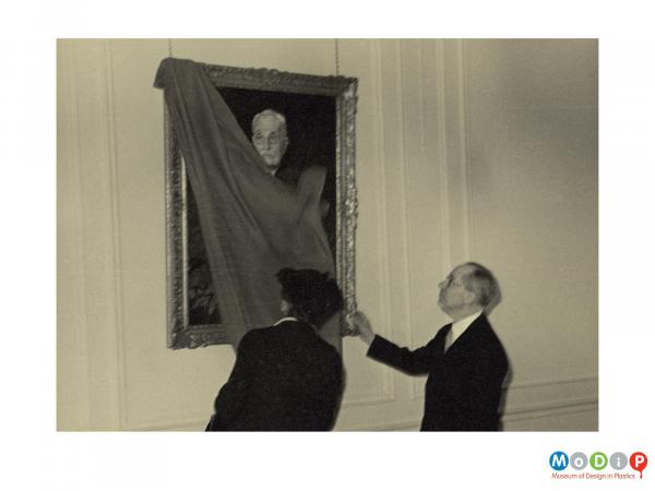 Scanned image showing a man and a woman removing a veil from a portrait.