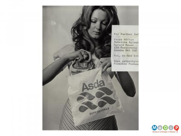 Scanned image showing a woman holding up an Asda shopping bag.