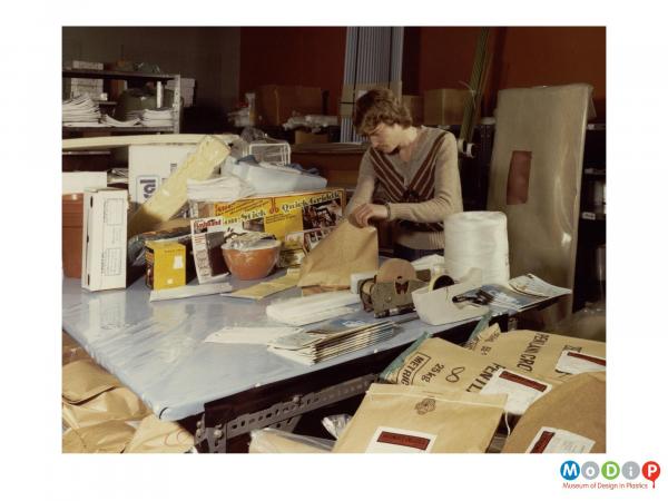 Scanned image showing a man packing items in a shop.