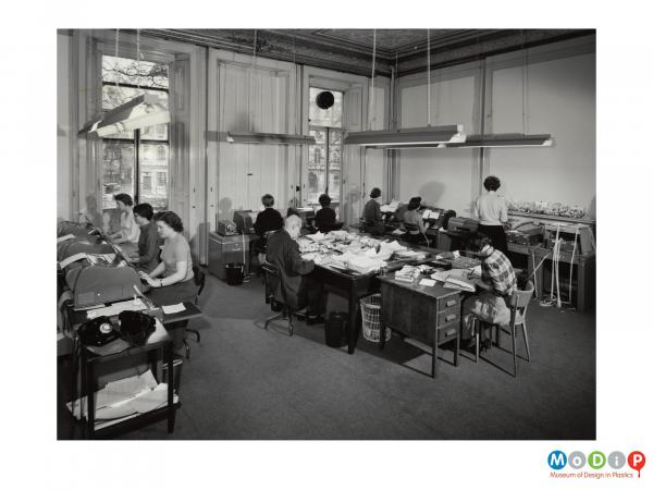 Scanned image showing an office filled with people and teleprinting machines.