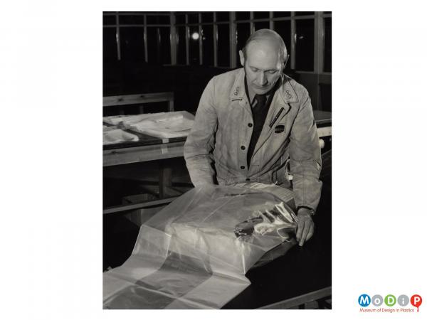 Scanned image showing a male post office worker covering a parcel with a plastic sack.