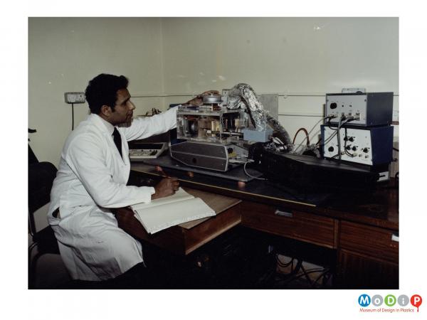 Scanned image showing a man in a white coat using a piece of testing equipment.