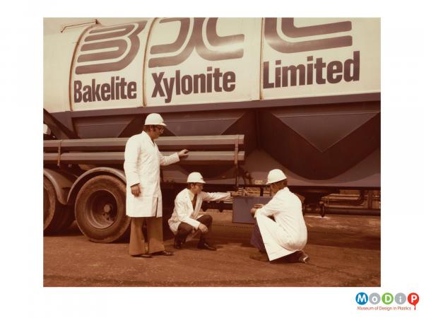 Scanned image showing three men in white coats and hard hats checking a tanker.