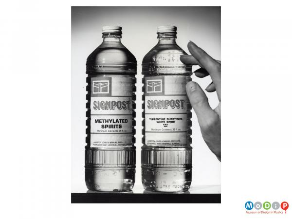 Scanned image showing a hand beside two clear bottles.