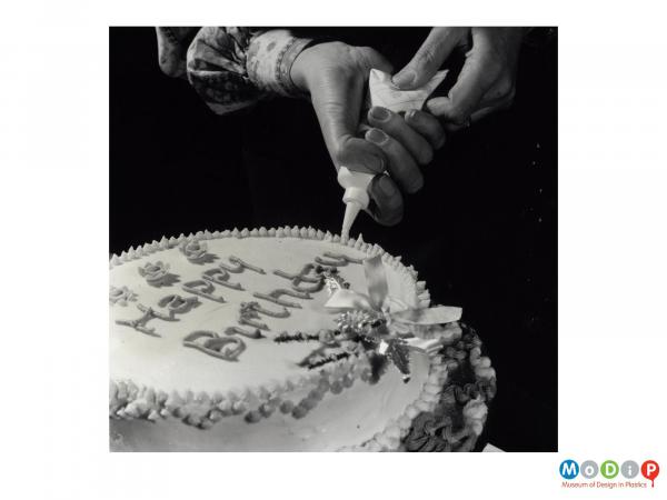 Scanned image showing someone decorating a cake.