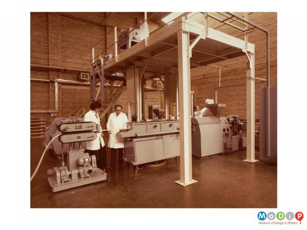 Scanned image showing workers at an extruding machine.