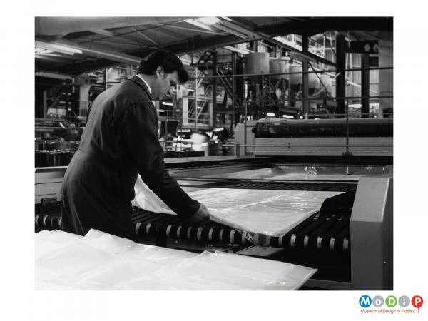 Scanned image showing a man at a bag making machine.