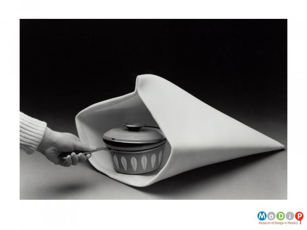 Scanned image showing a cooking pan being held by the handle and placed inside a padded bag.