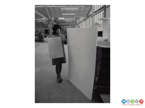 Scanned image showing a woman holding a sheet of material whilst standing next to the expanded equivalent.