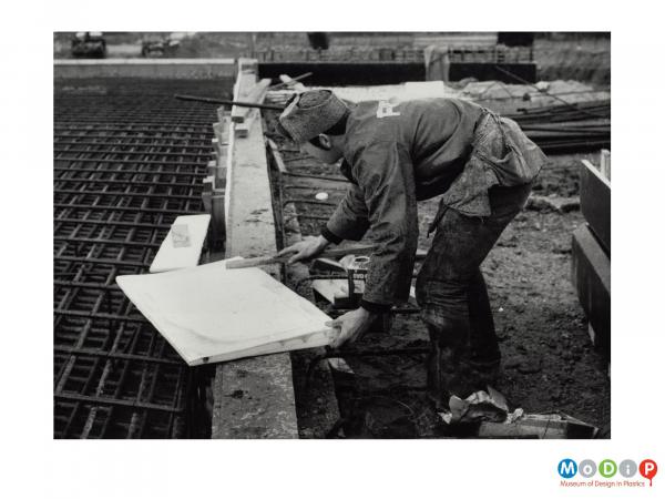 Scanned image showing a construction worker coating a wedge of plastazote before it is used as part of a bridge.