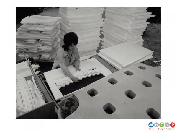 Scanned image showing a female worker removing cut sections from a sheet of Plastazote.