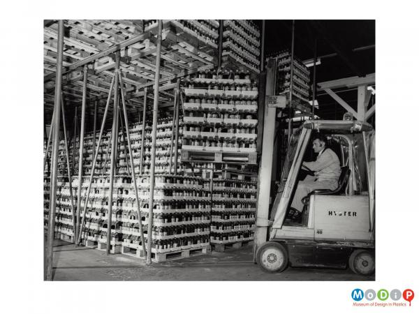 Scanned image showing a male employee using a forklift truck to move pallet loads of bottles.