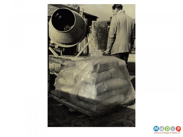 Scanned image showing a stack of building materials covered with polyethyne sheet.