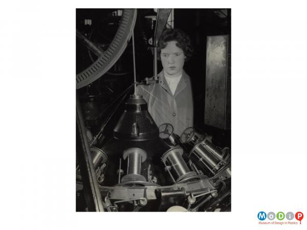 Scanned image showing a female employee at a wire braiding machine.