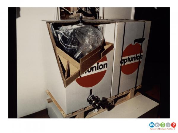 Scanned image showing two boxes with taps towards the base to dispense liquid.  One box has a corner removed to reveal the bag inside.
