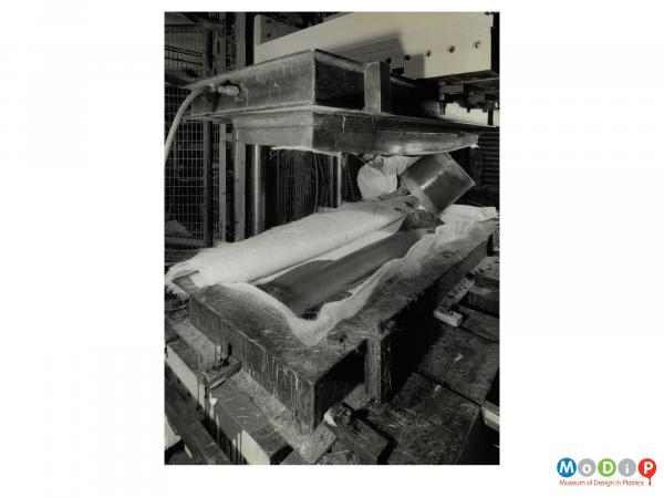 Scanned image showing a male worker pouring resin into a mould lined with glass fibre sheets.