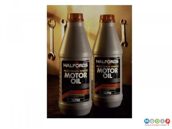 Scanned image showing two bottles of motor oil in front of a several spanners hanging on a wall.