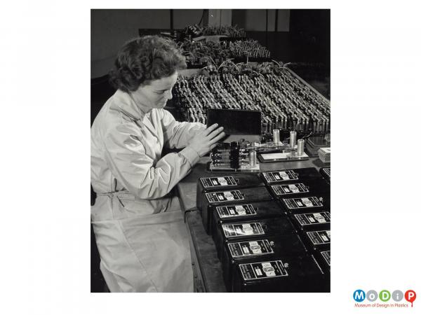 Scanned image showing a female worker putting covers on electrical equipment.