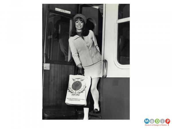 Scanned image showing a woman stapping off a train with a carrier bag.