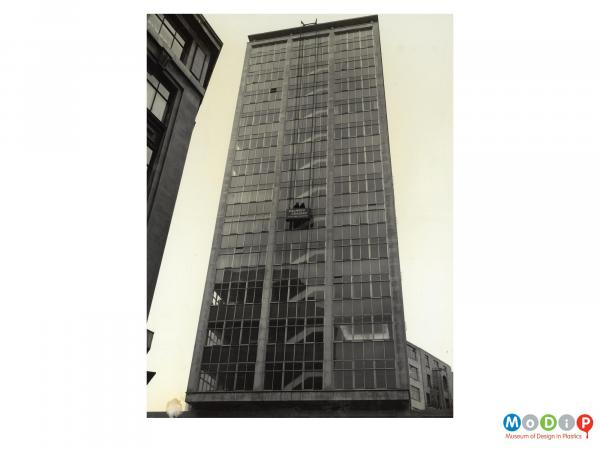 Scanned image showing a cradle on the side of a tall building.