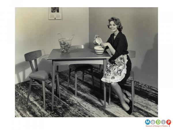 Scanned image showing a female modelling a dining table and chairs.