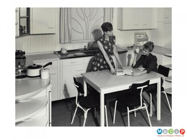 Scanned image showing two females modelling a fitted kitchen.