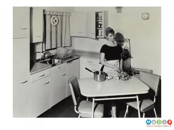 Scanned image showing a female modelling a fitted kitchen.