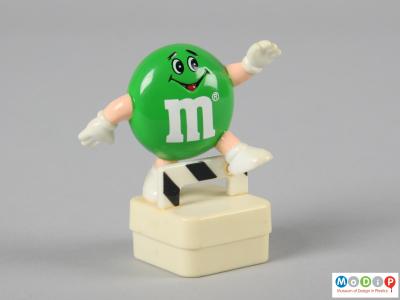 Front view of a green M&M figure showing the smiling face and the limbs.