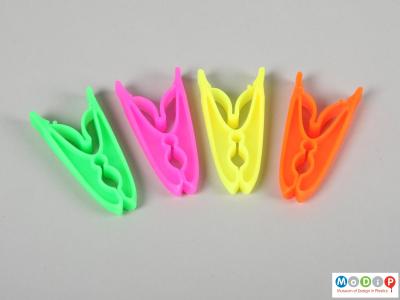 Side view of a packet of clothes pegs showing four pegs, one of each colour.