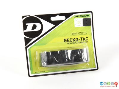 Front view of a packet of racket tape showing the packaging including a sample of the tape attached to the top corner.